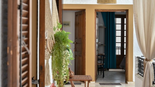 A spacious living area with a wooden floor, a hanging woven light fixture, and a view into another room through an open doorway. - Eva Studios & Apartments by Cretan Houses (Malevizi)