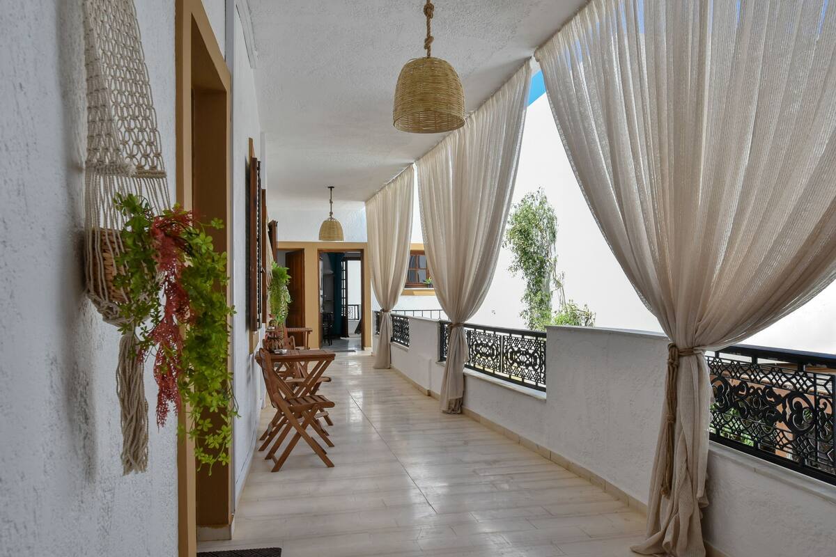 A balcony with a wooden floor, white walls, and a hanging woven light fixture.