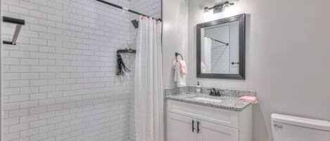 A bathroom with a shower, a sink with a mirror, and a toilet.