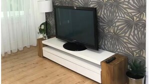 A modern living room with a flat-screen TV on a white console, a patterned wall, a wooden floor, and a potted plant. - Premium apartment with balcony (Ravensburg)