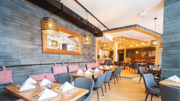 A modern restaurant with wooden tables and grey upholstered chairs, a patterned wall, and a large mirror. - Apartment for 6 in Fieberbrunn (Fieberbrunn)