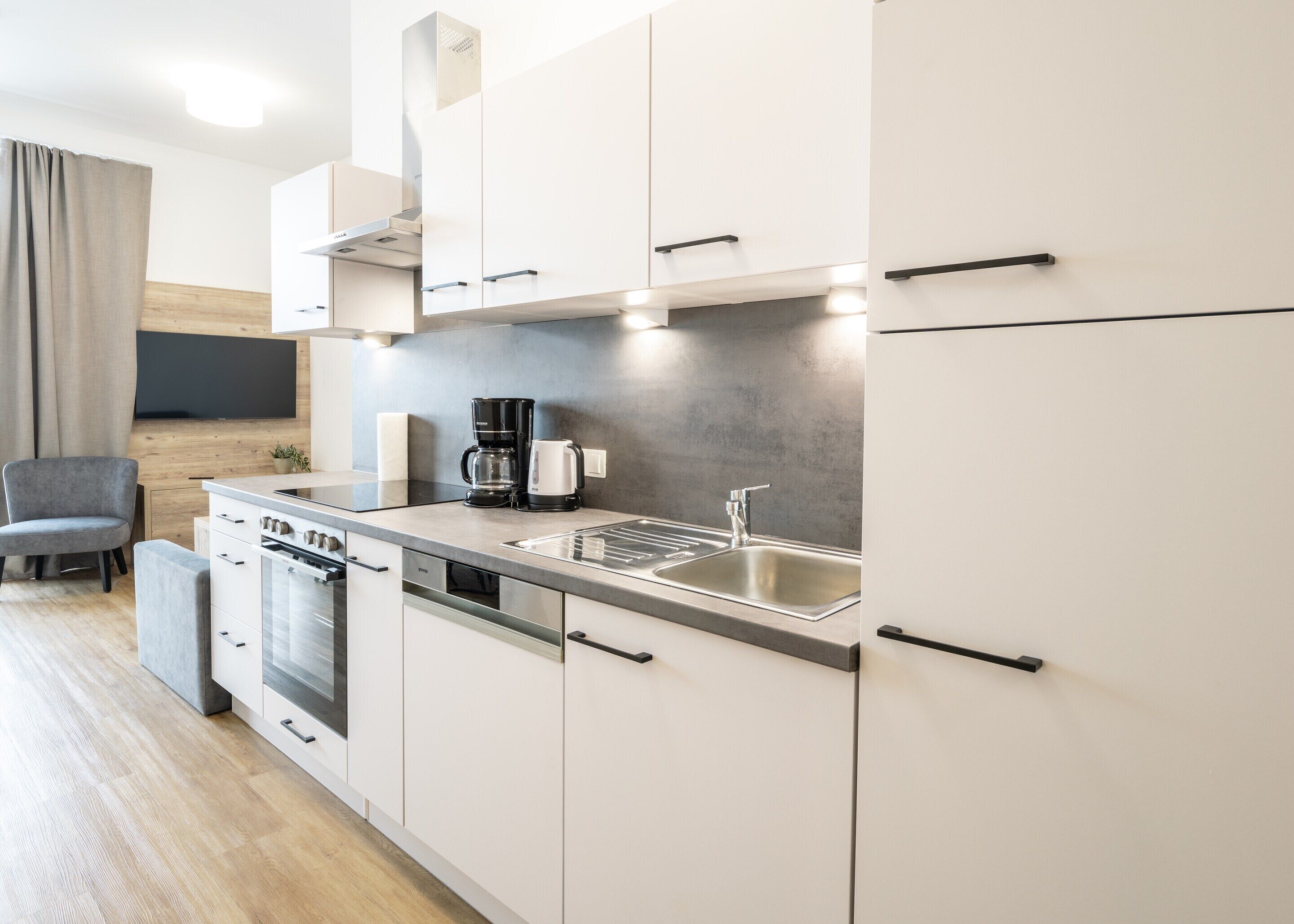A modern kitchen with white cabinets, a stainless steel sink, a coffee maker, and a dishwasher.
