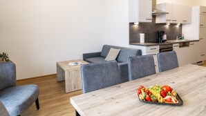 A modern apartment with a dining area, a gray sofa, a wooden coffee table, and a kitchen with white cabinets and a stainless steel range hood. - Apartment for 6 in Fieberbrunn (Fieberbrunn)