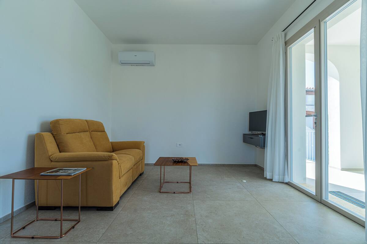 Un salon moderne comprenant un canapé, une table basse, un téléviseur à écran plat et une porte-fenêtre coulissante donnant sur l’extérieur.