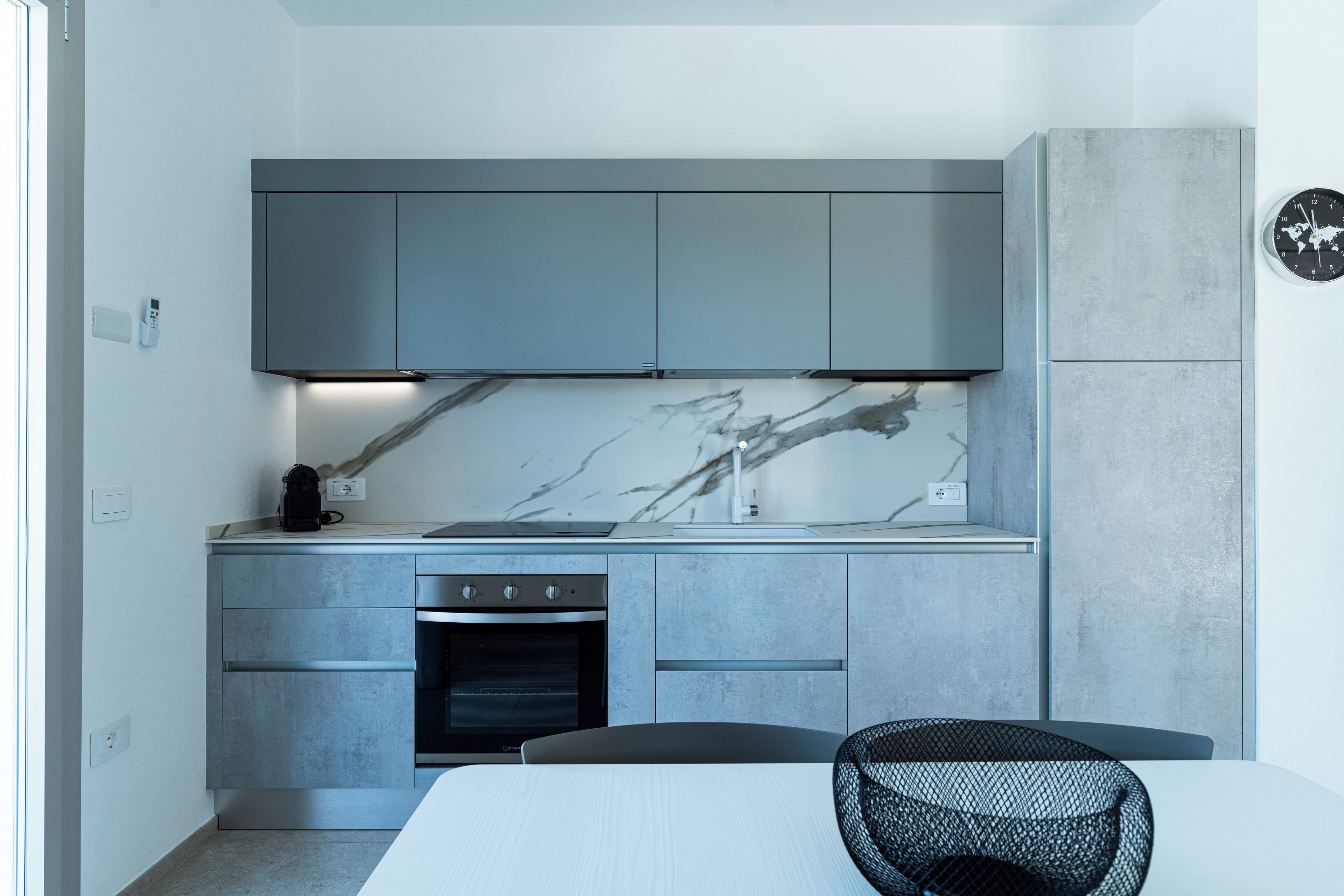Une cuisine moderne avec des meubles gris, un pare-feu en marbre et un four encastré.