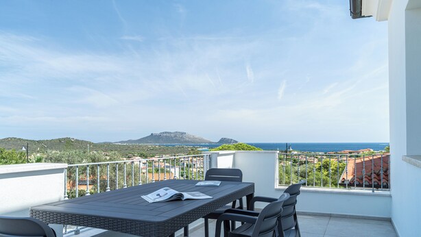 Un balcon avec une table et des chaises, offrant une vue panoramique sur la mer et les collines.