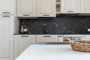 Una cocina moderna con armarios de madera clara, un protector contra salpicaduras de mármol negro y una estufa de acero inoxidable.