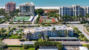 Un complex hoteler a la costa amb diversos edificis, una platja i una pista de tennis.