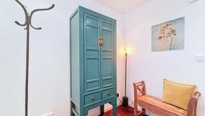 Ett turkost skåp med lådor, en golvlampa, en träbänk med en kudde och en tavla som hänger på väggen.
