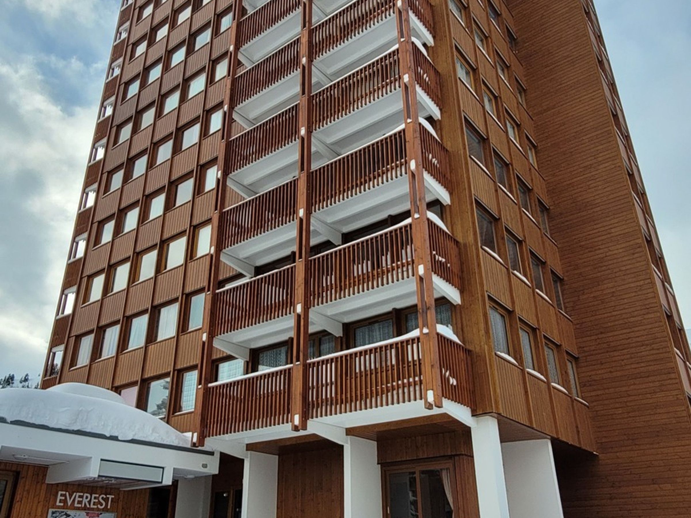 Um edifício de vários andares com fachada de madeira, varandas e uma placa com a inscrição 