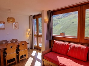 Um quarto com uma mesa de jantar de madeira, um sofá vermelho e uma grande janela com vista para uma paisagem verde.