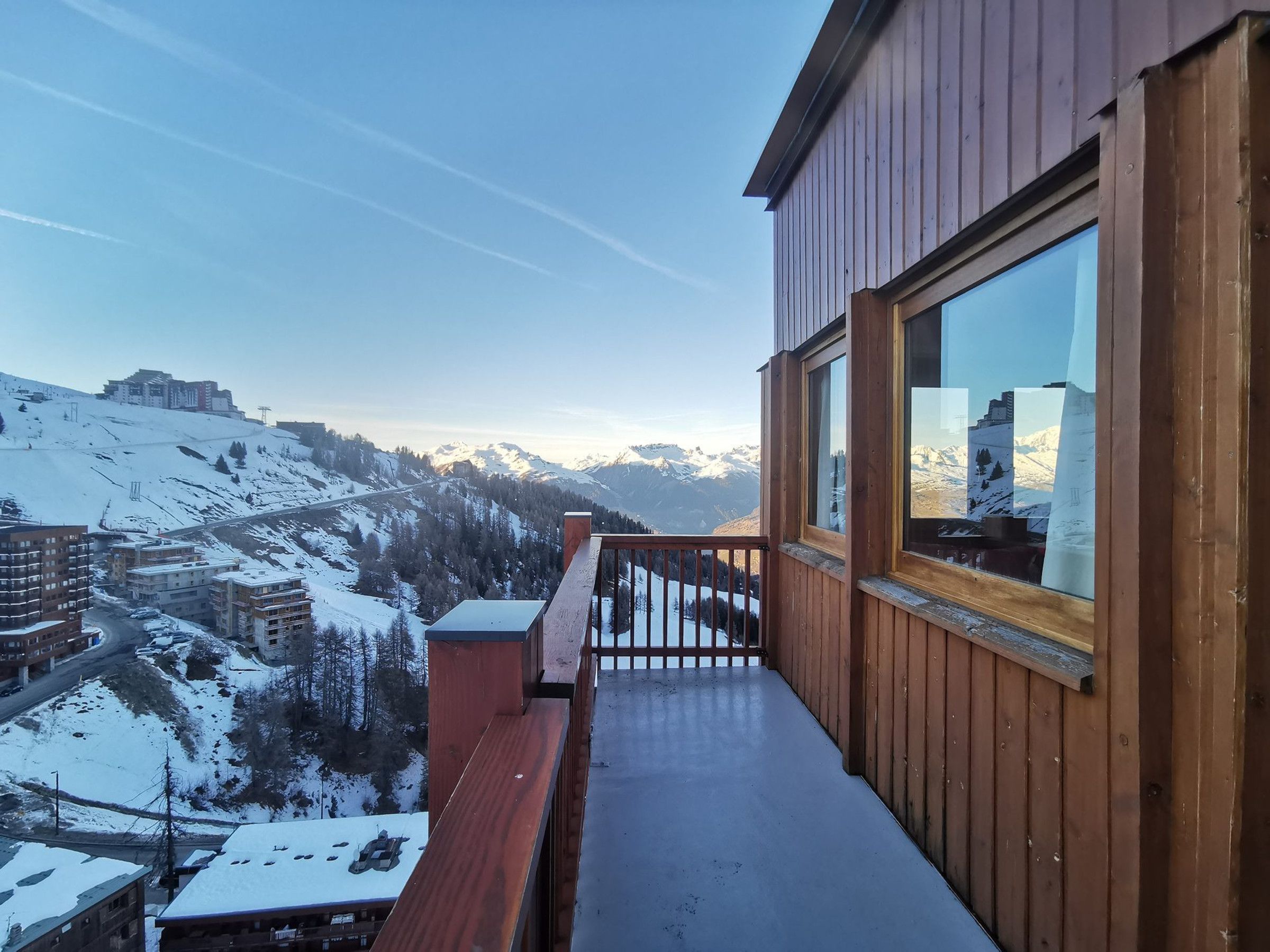 Un balcon en bois offrant une vue sur des montagnes enneigées et sur une ville située en contrebas.