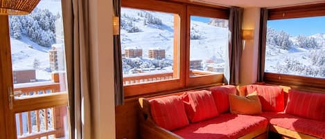 A cozy room with a wooden sofa, a small table, and large windows offering a snowy mountain view.