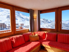 A room with a wooden bench and a view of snow-covered mountains.