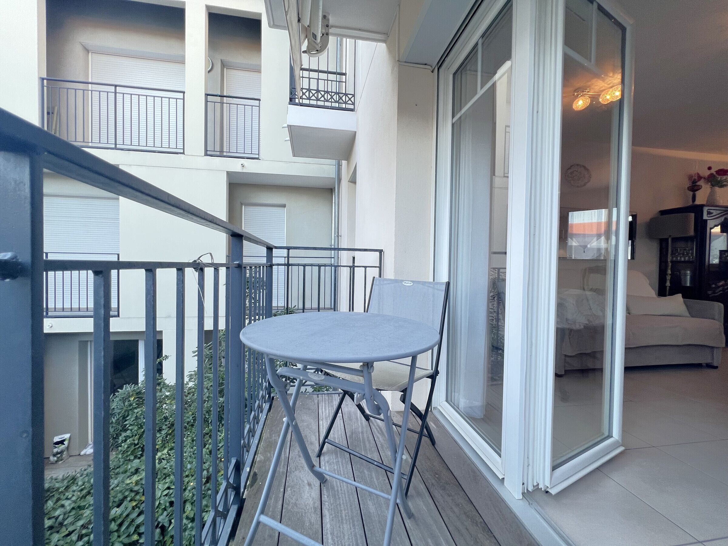 A balcony with a table and chairs, a sliding glass door leading to a living area, and a view of a building in the background.