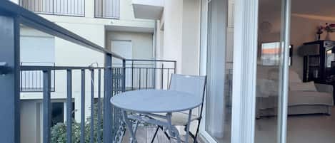 A balcony with a table and chairs, a sliding glass door leading to a living area, and a view of a building in the background.