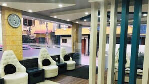 A modern waiting area with white cushioned seating, a clock on the wall, and a view of the street outside. - Joy Lux Stay (Anekal)