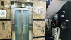 An elevator with a glass door, a sign indicating food availability, and a staircase with a handrail. - Joy Lux Stay (Anekal)