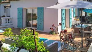 Una villa blanca con contraventanas azules, un patio con mobiliario exterior y una piscina.