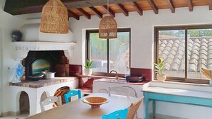Una cocina con chimenea de ladrillo, una mesa de comedor con sillas y lámparas de mimbre colgantes.