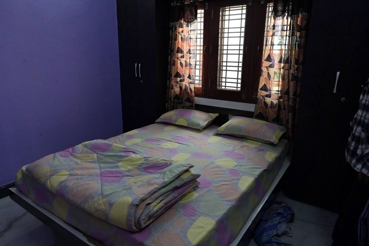 Un dormitorio con cama, paredes moradas y cortinas estampadas.