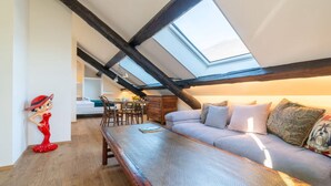 A loft-style room with a high ceiling, exposed wooden beams, a skylight, a sofa, a bench, and a decorative statue. - Luxury Suite Sunrise in Losone (Losone)