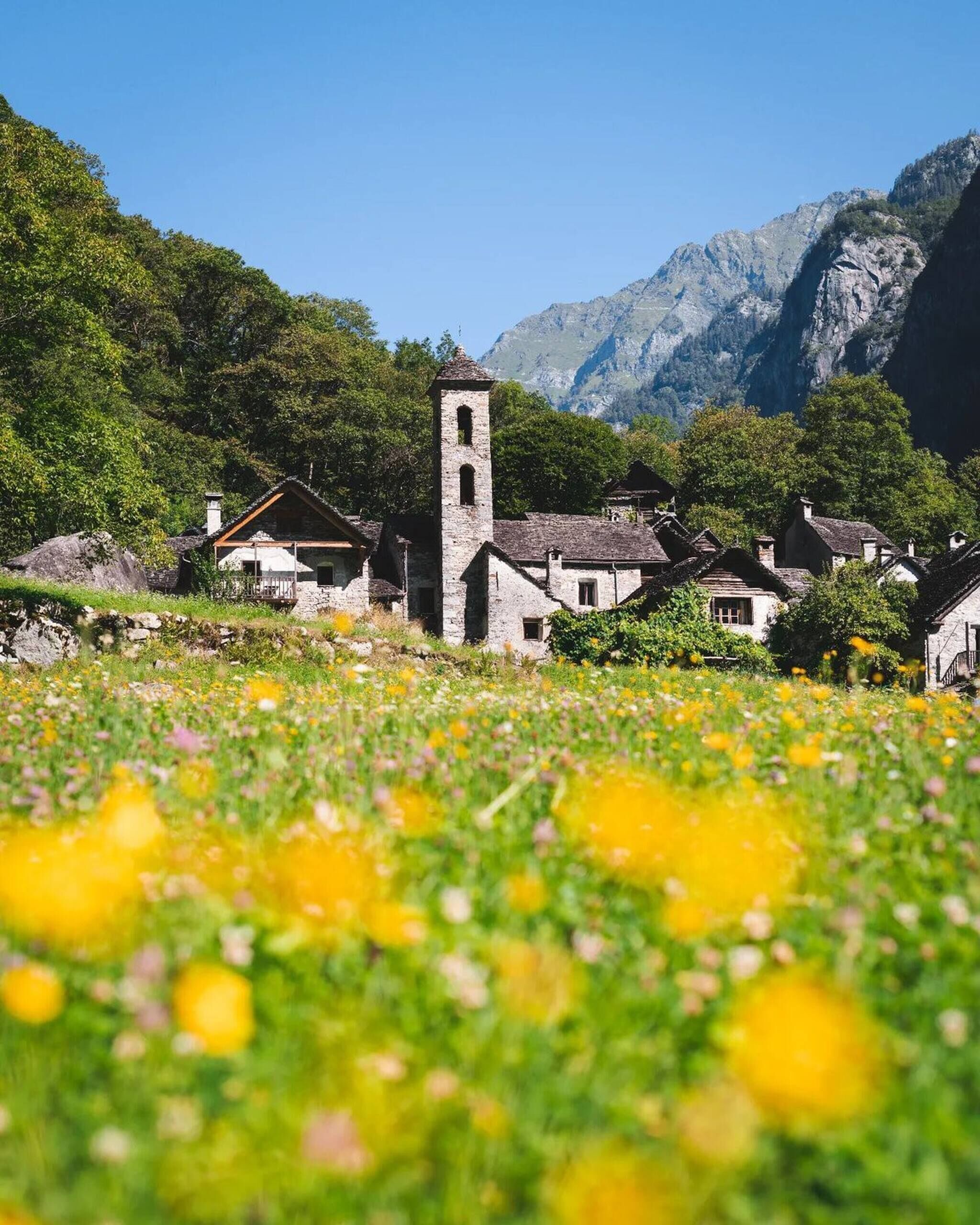 Ein Dorf mit traditionellen Steinbauten, einem markanten Kirchturm und einer bergigen Kulisse.