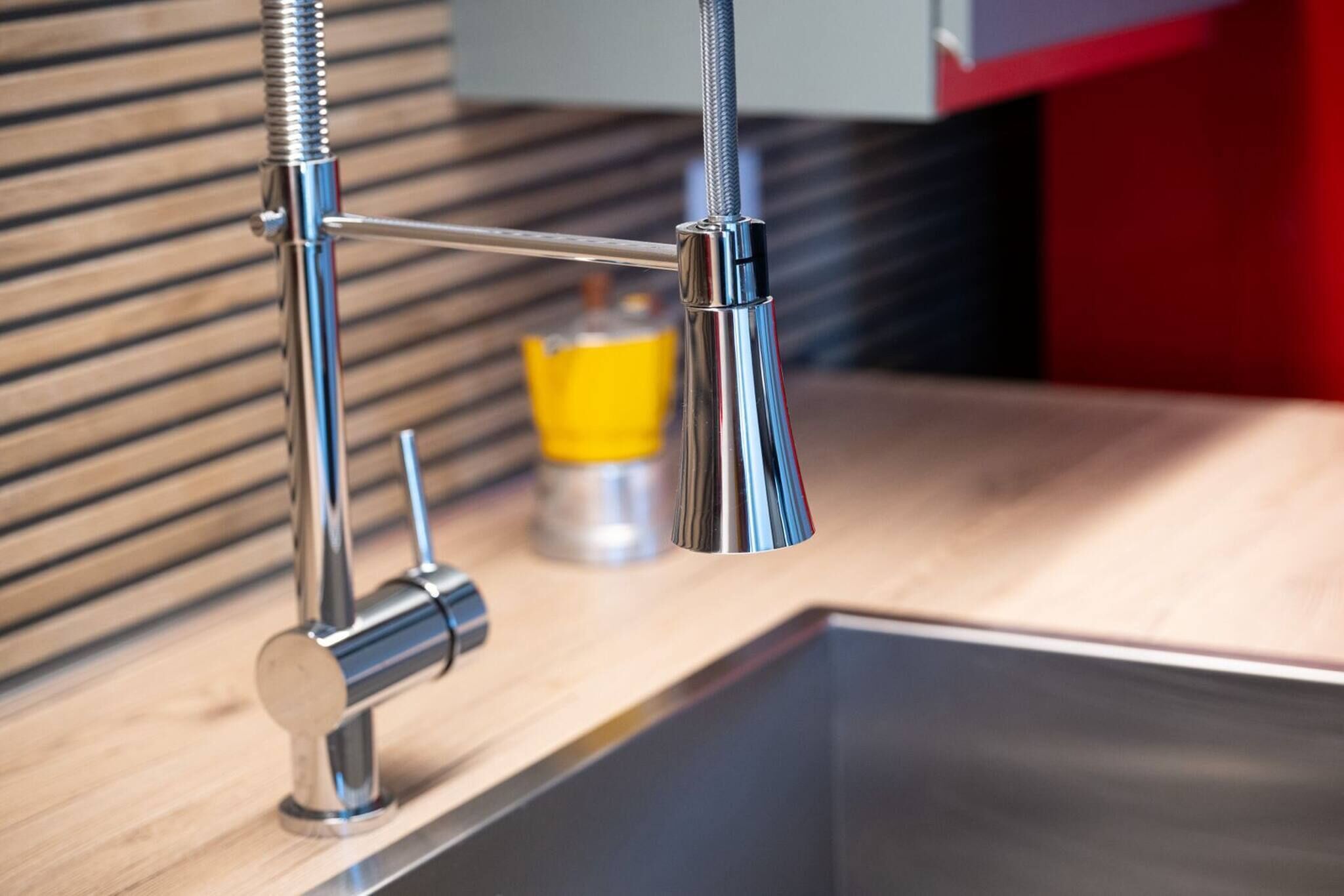 A modern kitchen with a stainless steel faucet, a wooden countertop, and a yellow bottle in the background.