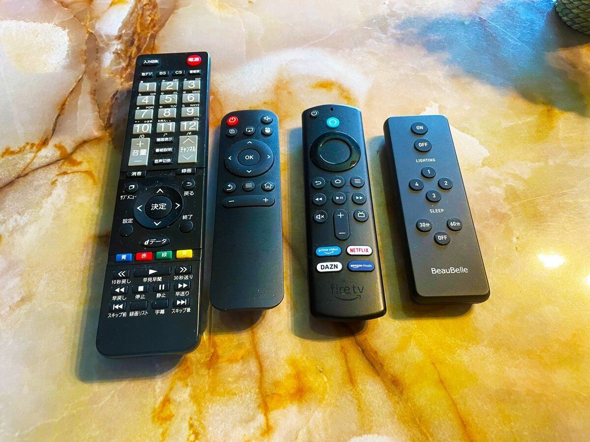 Four remote controls on a marble surface.