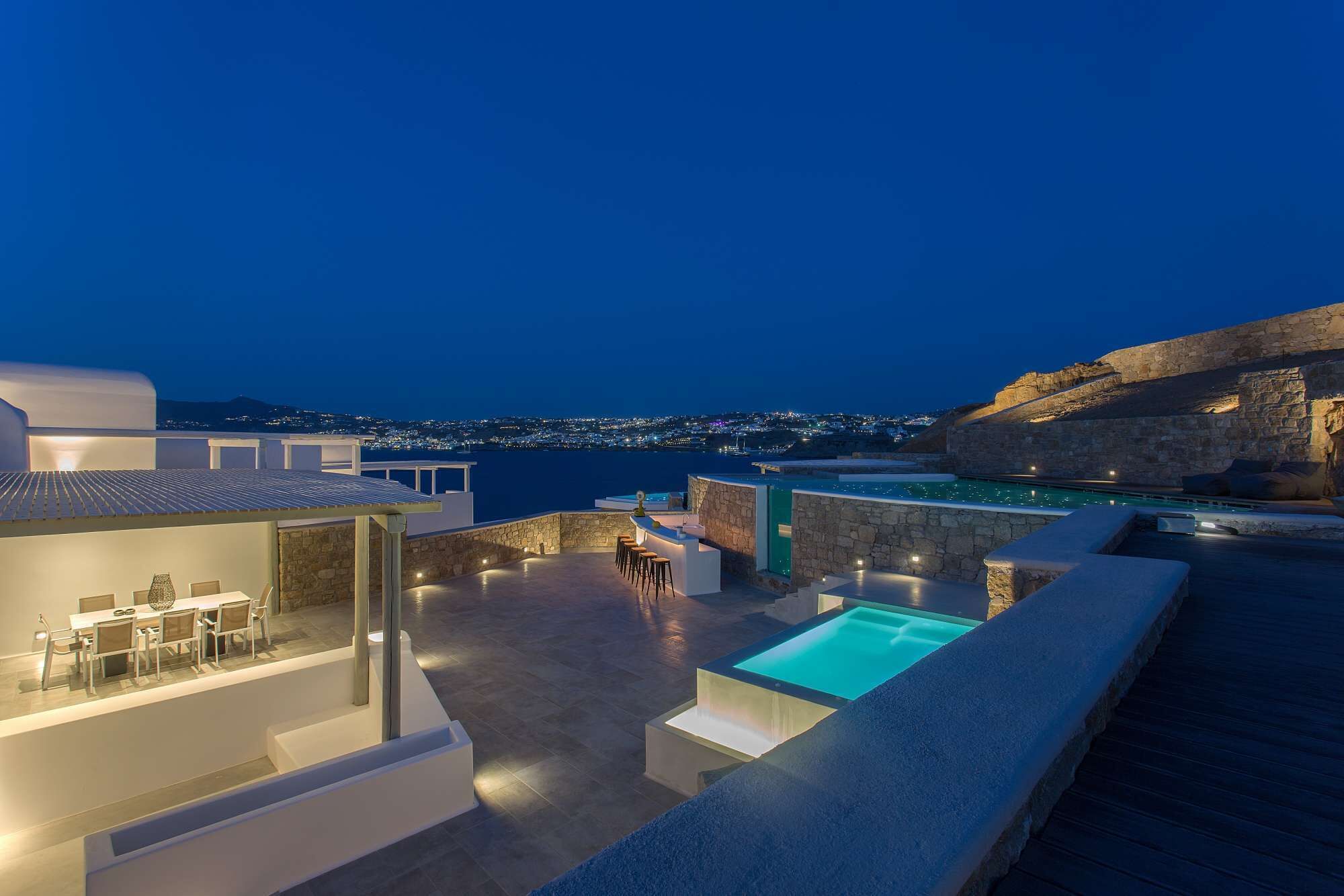 A rooftop terrace with a pool, dining area, and a view of the city at night.