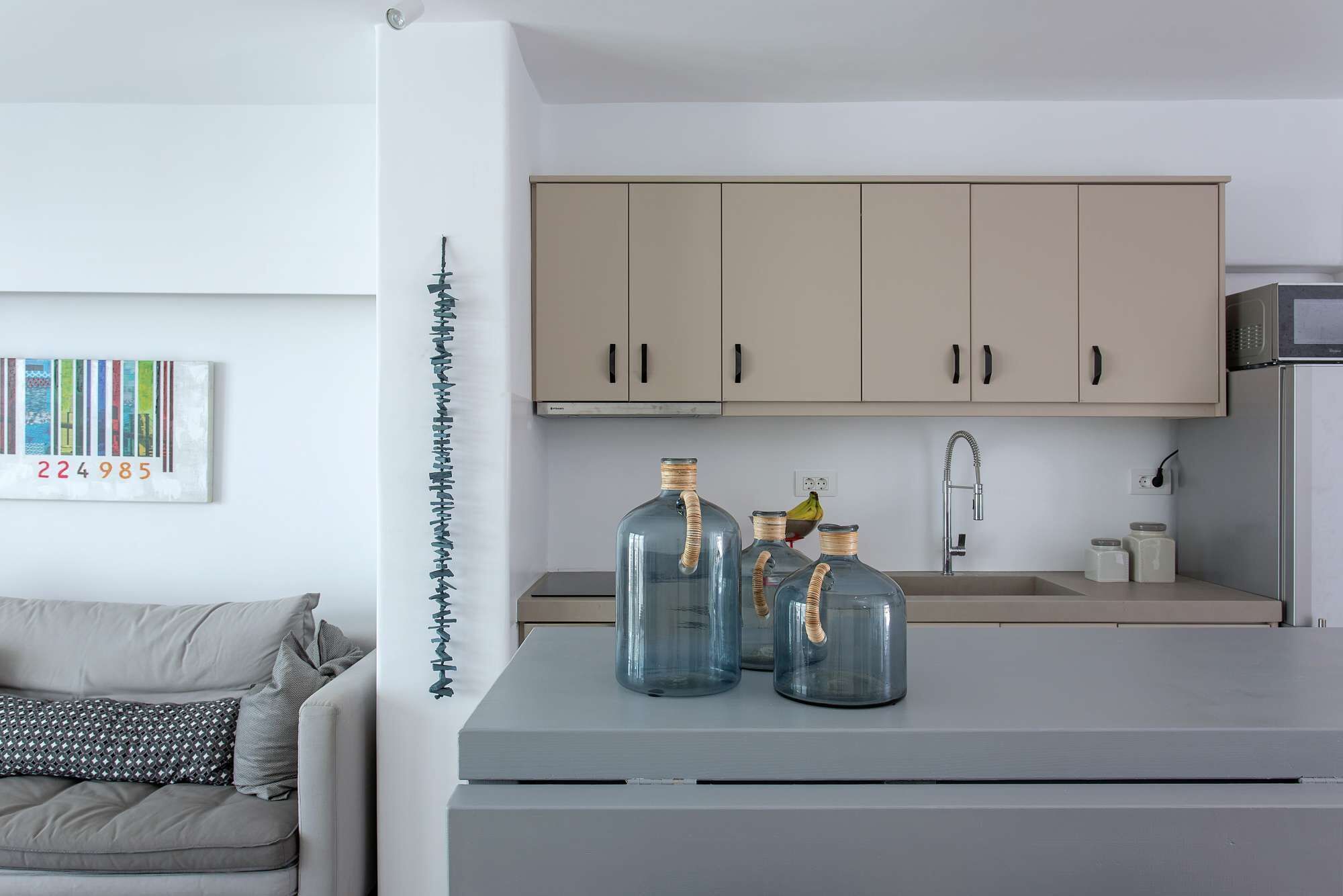 Une cuisine moderne avec des meubles de couleur claire, un plan de travail gris et trois bocaux en verre avec des bandes métalliques.