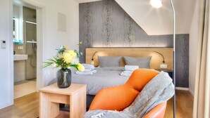 Een moderne slaapkamer met een geruit beddegoed, een houten hoofdbord, een nachtkastje met een bloevas en een oranje fauteuil.