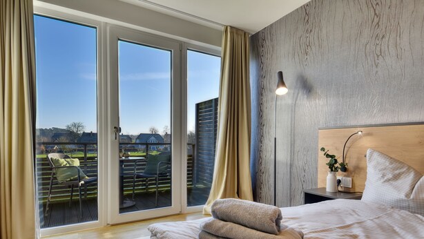 Une chambre avec une grande fenêtre, un lit, une table de chevet et une vue sur l’extérieur.