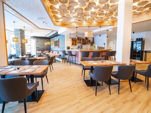 Un intérieur de restaurant moderne avec un plancher en bois, des chaises à revêtement gris et un bar doté d’un comptoir en bois.