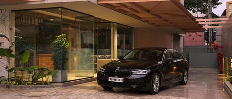 A black car parked in front of a building with a glass entrance and a wooden overhang.