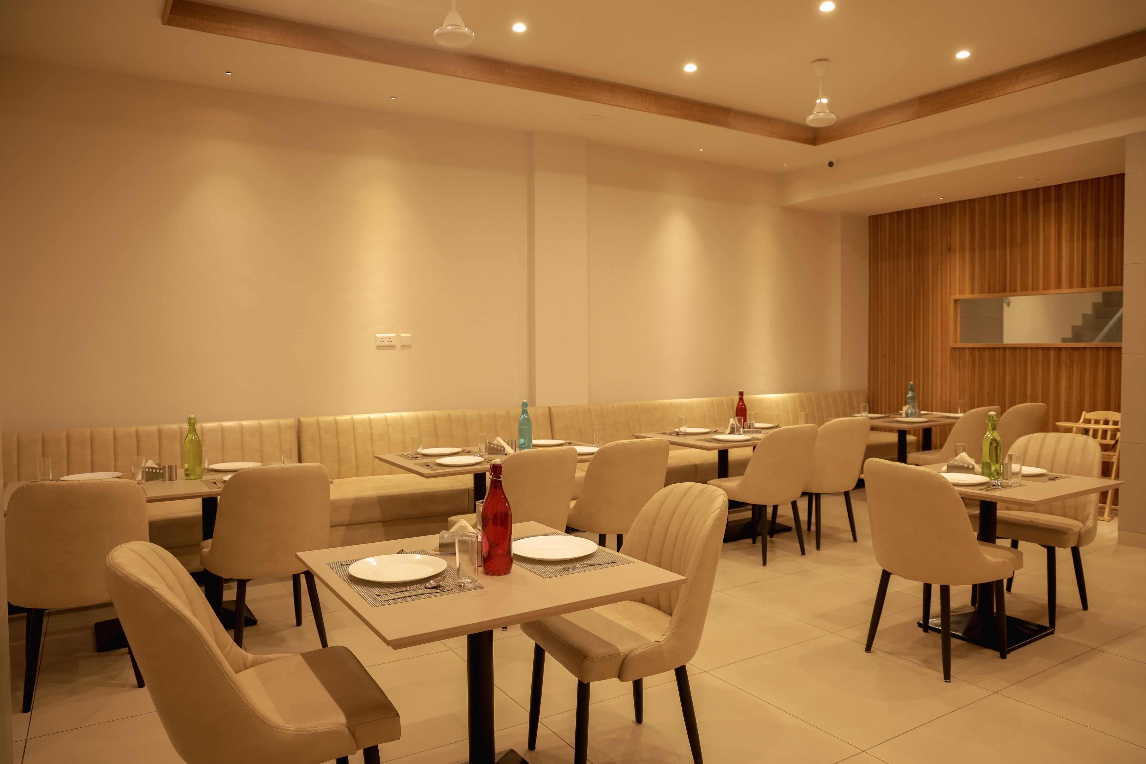 Un comedor moderno con varias mesas y sillas, un revestimiento de pared de madera e iluminación empotrada en el techo.