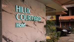 A hotel entrance with a sign reading "Hilux Courtyard Hotel" and a black car parked outside. - Hilux Courtyard (Palakkad)