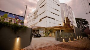A modern hotel with a curved facade and a car parked in front. - Hilux Courtyard (Palakkad)