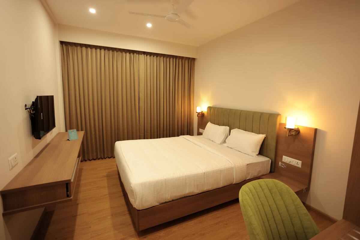 A hotel room with a bed, a desk, a television, and a green chair.