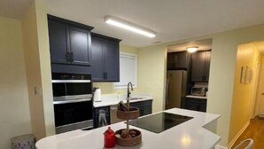 A modern kitchen with a central island, white chairs, dark cabinets, and a stainless steel refrigerator. - Vacation getaway (Morehead City)