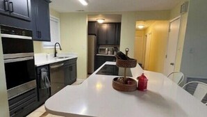A compact kitchen with dark cabinets, a white countertop, and a dining area with a white table and chairs. - Vacation getaway (Morehead City)