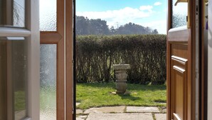 An open door revealing a garden with a stone planter and a hedge.
