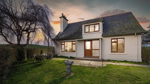 A two-story house with a well-maintained lawn, a stone pillar, and a dining area with chairs.