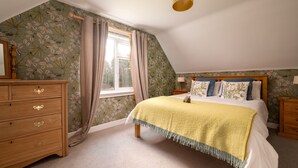 A bedroom with a sloped ceiling, a wooden dresser, a bed with a yellow blanket, and floral wallpaper.
