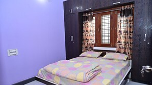 A bedroom with a bed, purple walls, a window with curtains, and a wardrobe. - Mayur Shines (Anekal)