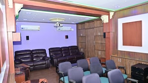 A room with a large screen, leather seating, and a ceiling fan. - Mayur Shines (Anekal)