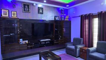 Una sala de estar con un televisor de pantalla plana grande, un sofá, una mesa de centro y un mueble con cuadros enmarcados.