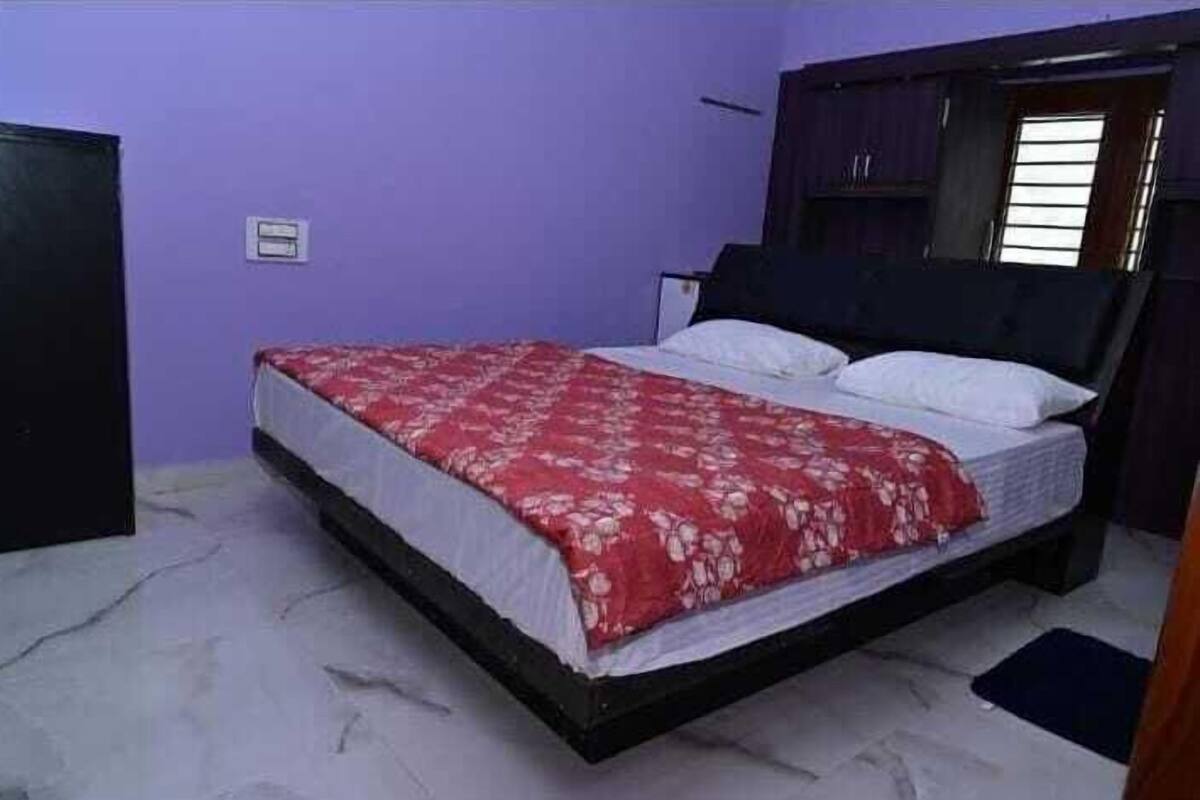 Una cama individual con una colcha roja estampada en una habitación con paredes moradas y suelo de mármol.