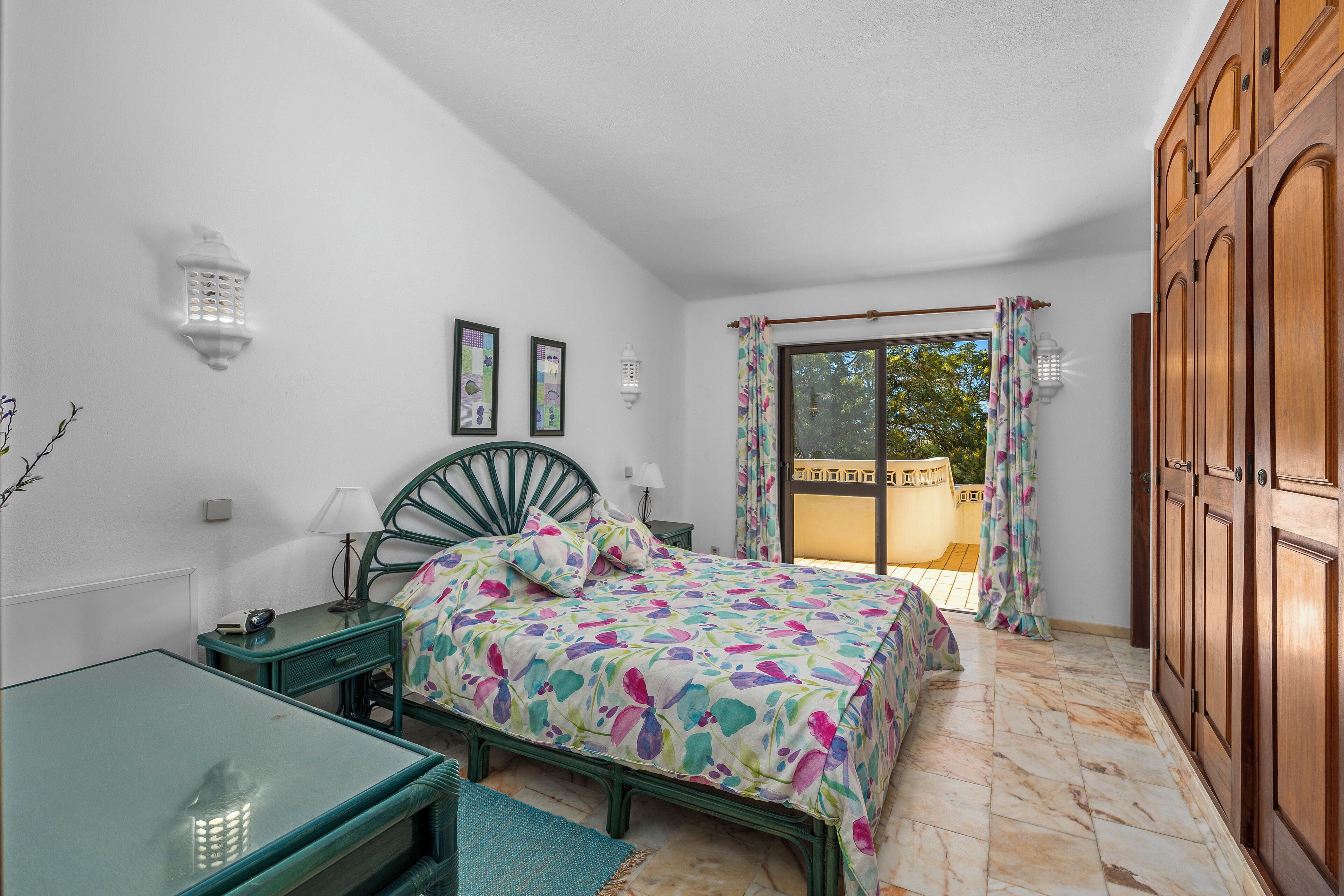 A bedroom with a bed, a desk, a chair, a wardrobe, and a window with curtains.