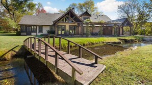 A house with a wooden deck over a stream, a covered outdoor seating area, and a large lawn. - Whispering Brook-Outdoor oasis w/stream-Sleeps 16 (Springdale)